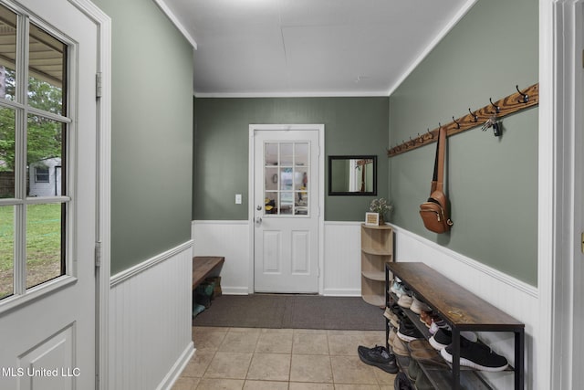 doorway featuring crown molding, tile patterned floors, and a wainscoted wall