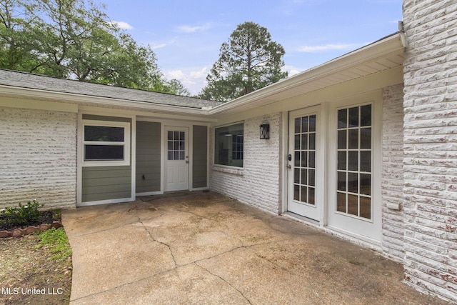 entrance to property featuring brick siding, a shingled roof, and a patio
