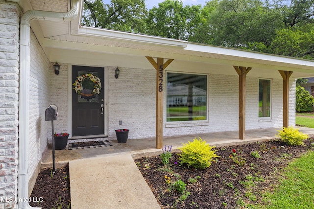 view of exterior entry featuring brick siding and covered porch