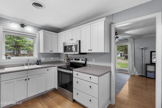 kitchen with crown molding, a sink, white cabinets, light wood-style floors, and stainless steel appliances