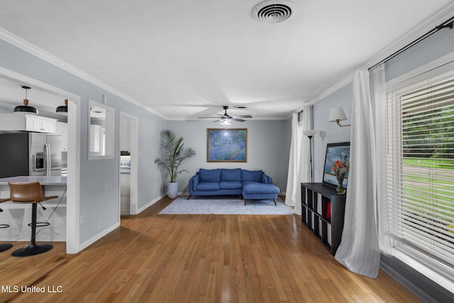living room featuring visible vents, ornamental molding, wood finished floors, baseboards, and ceiling fan