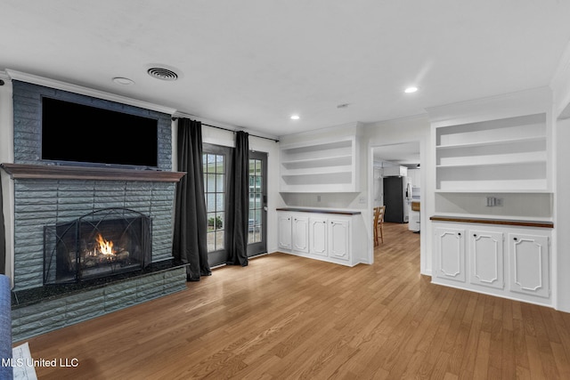 unfurnished living room with light wood-type flooring, ornamental molding, a brick fireplace, and visible vents