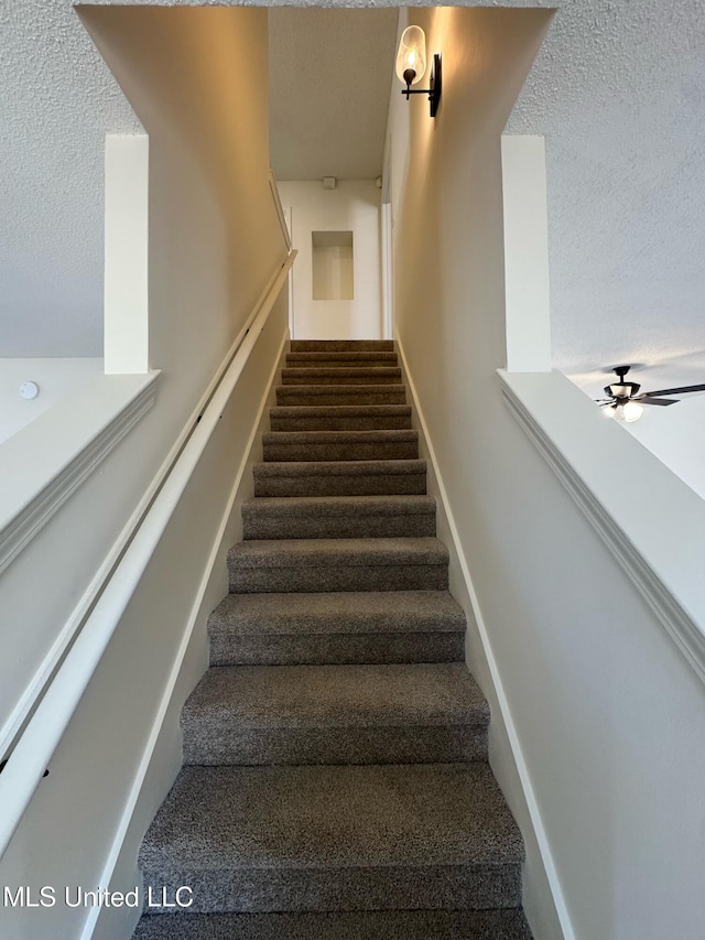 staircase featuring a textured ceiling and ceiling fan