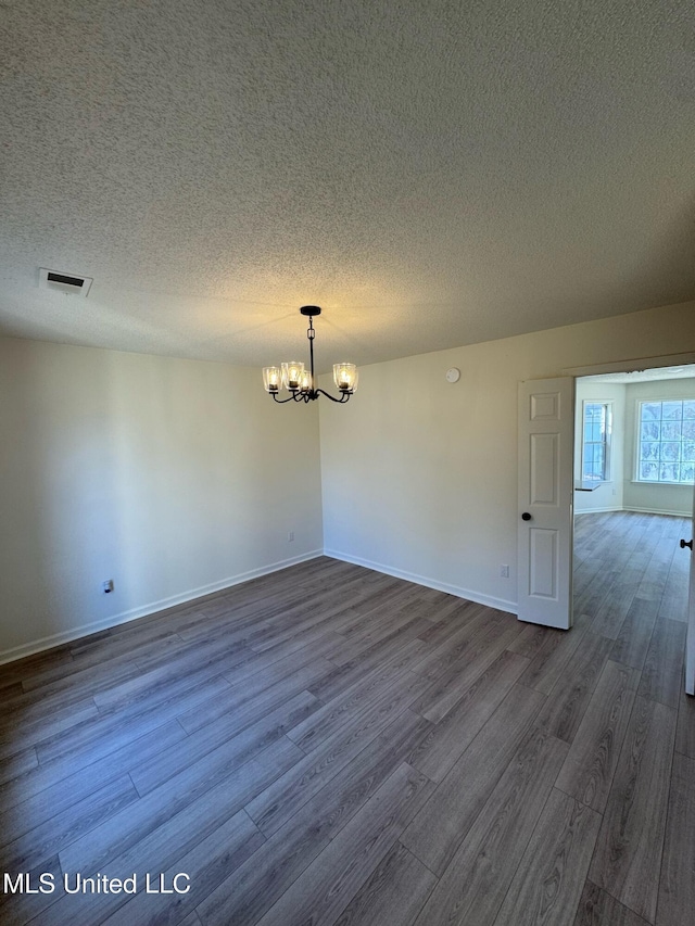 unfurnished room with a textured ceiling, a chandelier, and dark hardwood / wood-style floors