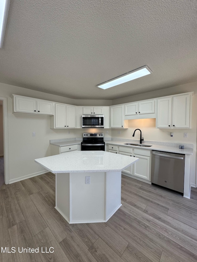 kitchen with stainless steel appliances, sink, light hardwood / wood-style flooring, white cabinets, and a kitchen island