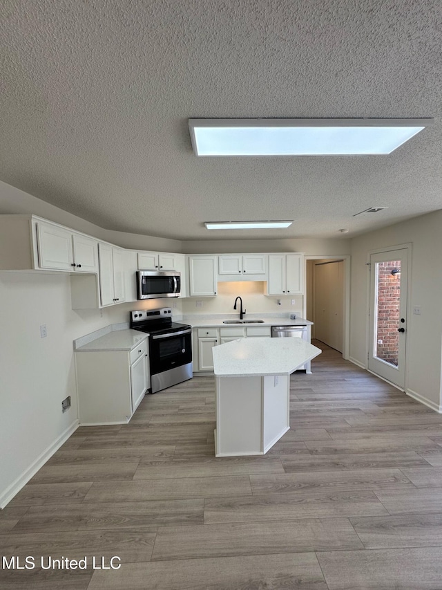 kitchen featuring a kitchen island, white cabinetry, stainless steel appliances, and a skylight