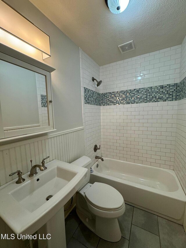 full bathroom featuring sink, a textured ceiling, tile patterned floors, toilet, and tiled shower / bath combo