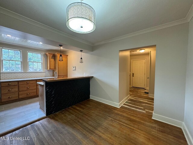 kitchen featuring dark wood-type flooring, crown molding, backsplash, and kitchen peninsula