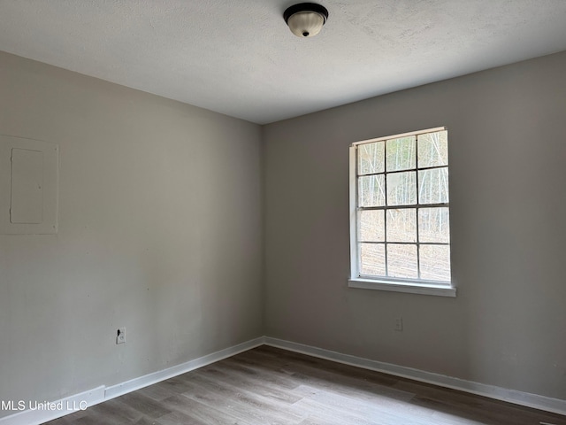 unfurnished room featuring electric panel, wood finished floors, baseboards, and a wealth of natural light