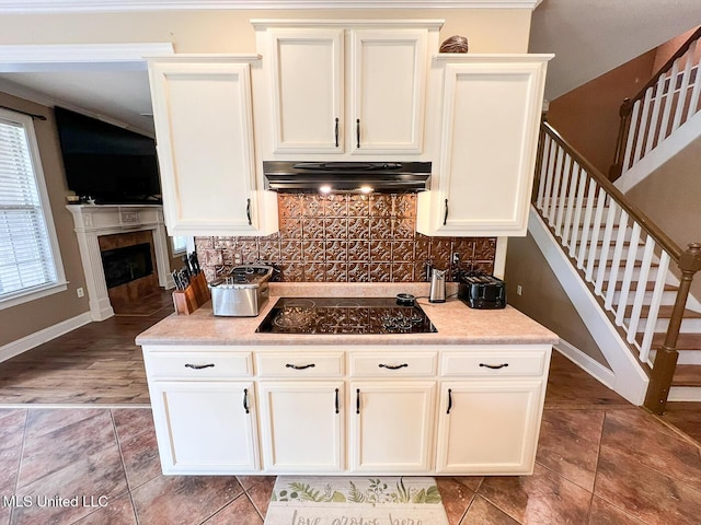 kitchen with exhaust hood, white cabinetry, baseboards, black stovetop, and tasteful backsplash