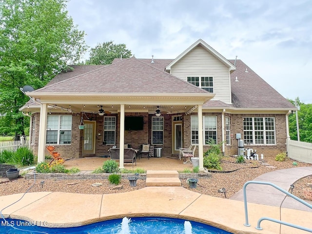 rear view of property with a ceiling fan, roof with shingles, brick siding, fence, and a patio