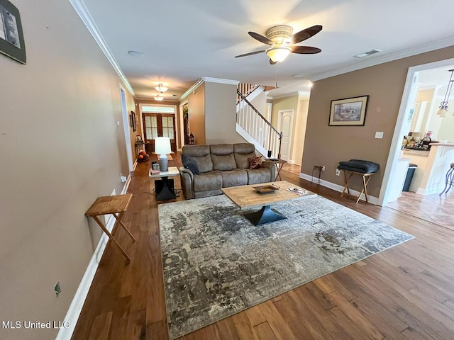 living room with a ceiling fan, wood finished floors, stairway, baseboards, and ornamental molding