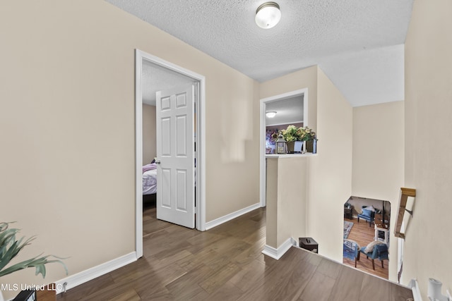hall featuring wood finished floors, a textured ceiling, and baseboards
