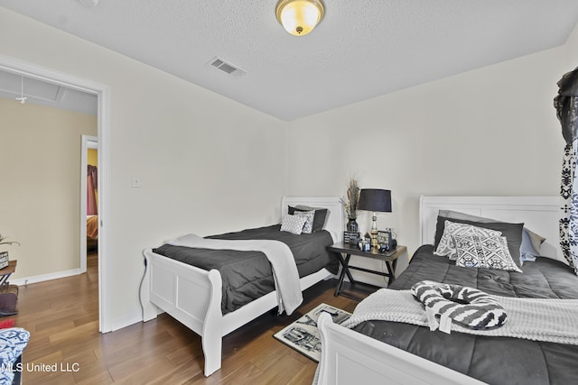 bedroom with attic access, wood finished floors, visible vents, and a textured ceiling