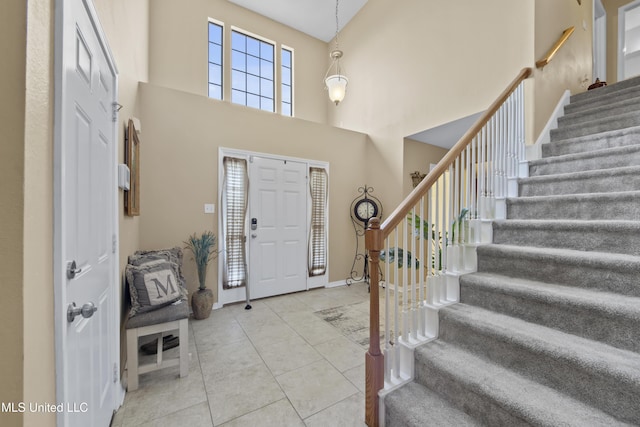 foyer with a towering ceiling, tile patterned floors, stairs, and baseboards