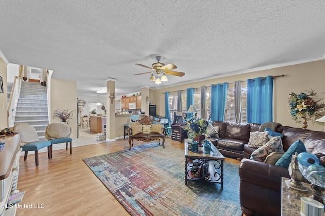 living room featuring light wood-style flooring, a textured ceiling, a ceiling fan, stairway, and ornamental molding