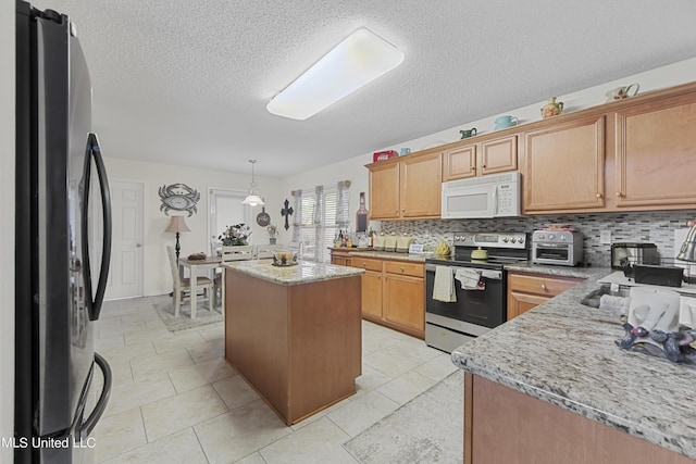 kitchen with freestanding refrigerator, a center island, white microwave, decorative backsplash, and stainless steel electric range oven