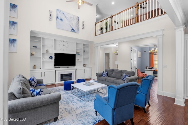 living room featuring decorative columns, dark hardwood / wood-style floors, a high ceiling, built in shelves, and ceiling fan with notable chandelier