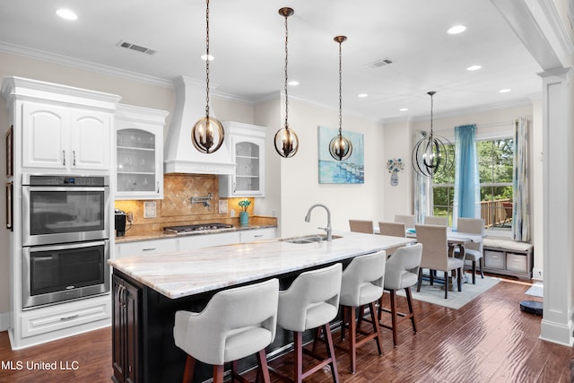 kitchen with white cabinets, an island with sink, appliances with stainless steel finishes, dark wood-type flooring, and sink