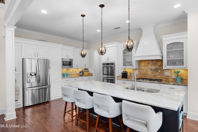 kitchen with white cabinetry, custom range hood, stainless steel appliances, and a center island with sink