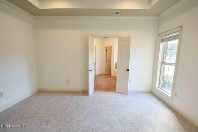 carpeted empty room with a raised ceiling, ornamental molding, and plenty of natural light