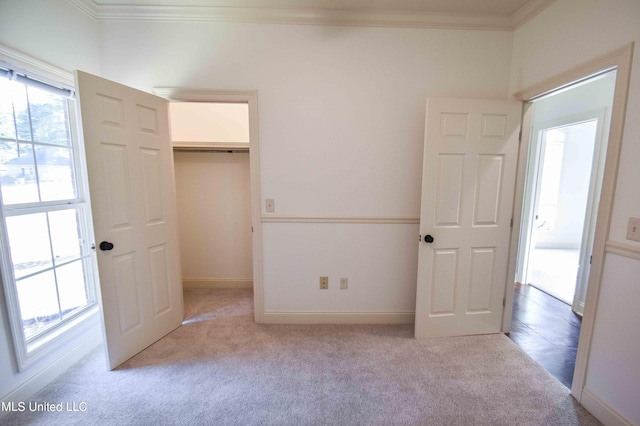 unfurnished bedroom featuring a spacious closet, crown molding, light colored carpet, and a closet