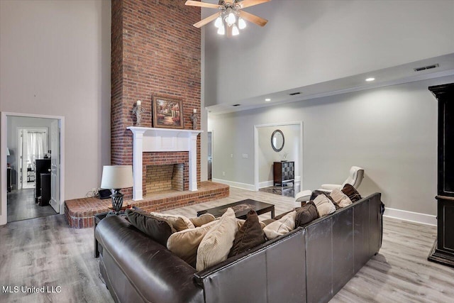 138 Oak Ridge Cir, Madison, MS 39110 - living room featuring a towering ceiling, ceiling fan, light wood-style floors, a brick fireplace, and baseboards