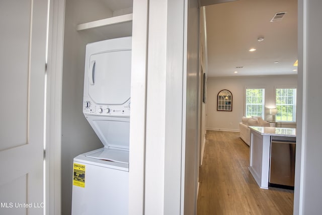 laundry area featuring light wood-type flooring, baseboards, stacked washer and dryer, laundry area, and recessed lighting