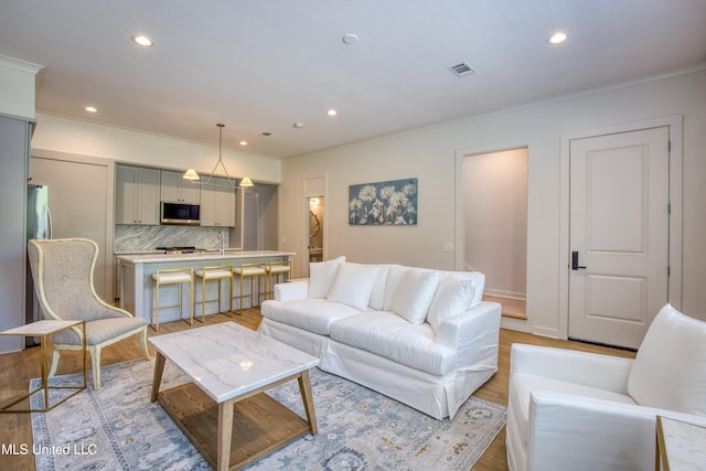 living area featuring crown molding, light wood finished floors, visible vents, and recessed lighting