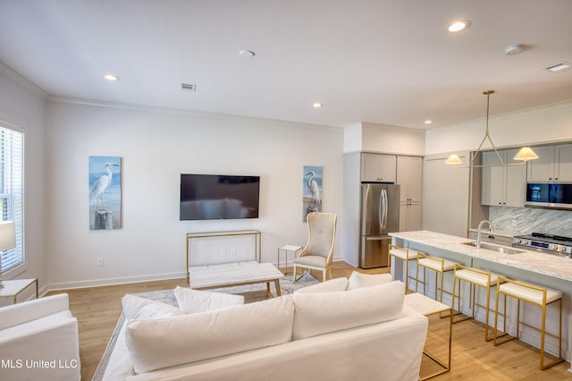 living area with ornamental molding, light wood-style floors, visible vents, and recessed lighting
