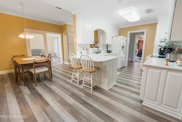 kitchen featuring white cabinets, white refrigerator with ice dispenser, decorative light fixtures, and light wood-type flooring