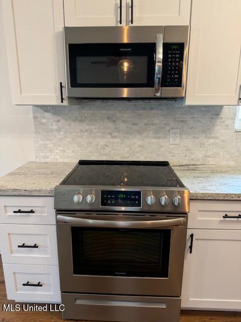 kitchen featuring stainless steel appliances, white cabinets, and light stone countertops