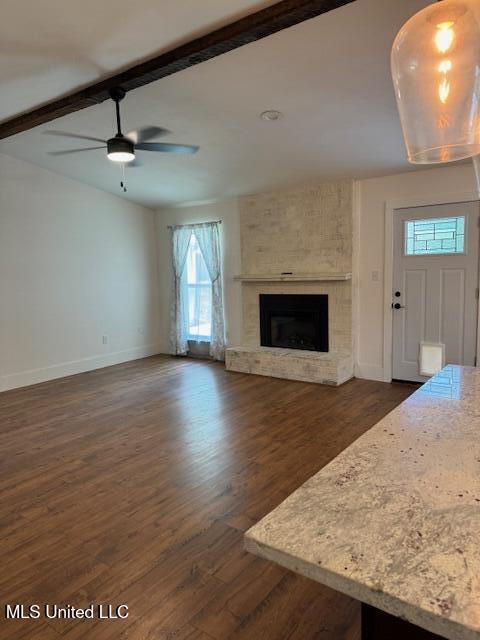 unfurnished living room featuring a fireplace, ceiling fan, beamed ceiling, and dark hardwood / wood-style floors