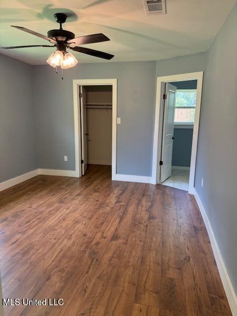 unfurnished bedroom with a closet, a walk in closet, ceiling fan, and wood-type flooring