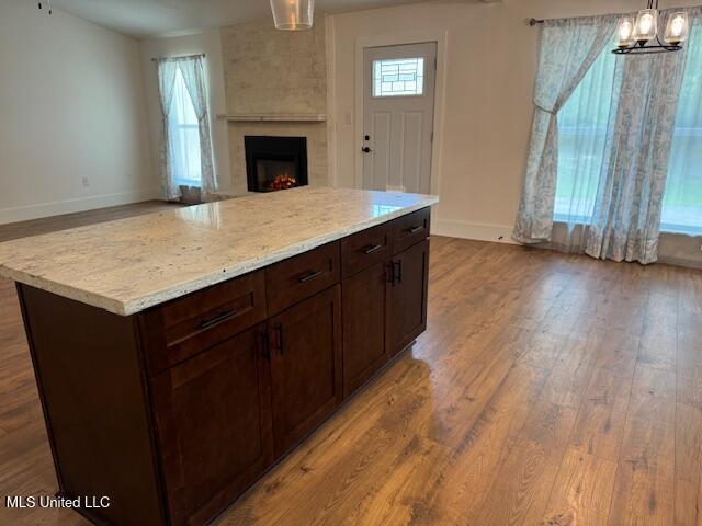 kitchen featuring decorative light fixtures, a fireplace, light hardwood / wood-style floors, light stone countertops, and a kitchen island