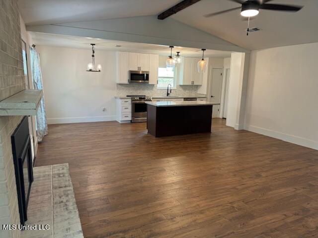 kitchen featuring appliances with stainless steel finishes, a center island, decorative backsplash, white cabinets, and decorative light fixtures