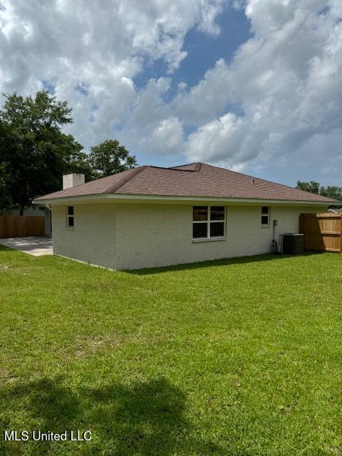 rear view of property featuring central air condition unit and a yard