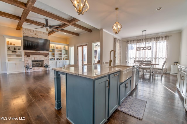 kitchen with coffered ceiling, beam ceiling, pendant lighting, light stone counters, and a center island with sink