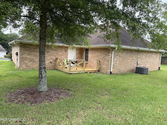 back of house featuring roof with shingles, central air condition unit, brick siding, a wooden deck, and a lawn
