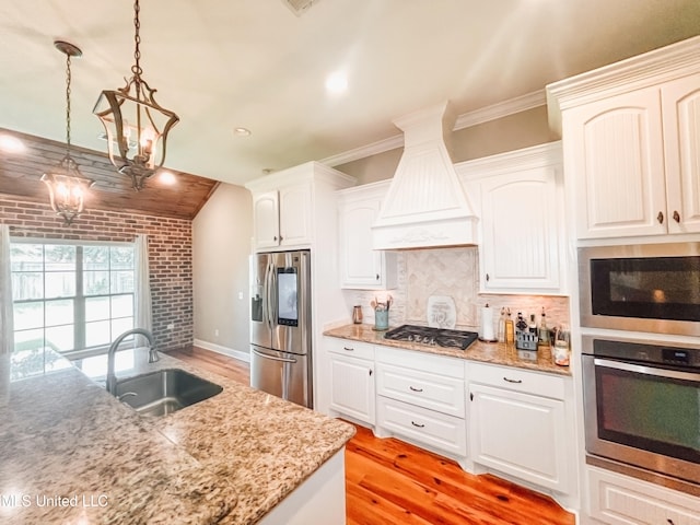 kitchen featuring pendant lighting, premium range hood, sink, white cabinetry, and stainless steel appliances