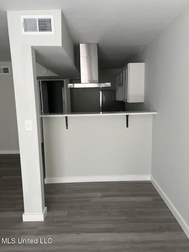 kitchen with wall chimney exhaust hood, white cabinets, a kitchen bar, and dark hardwood / wood-style flooring