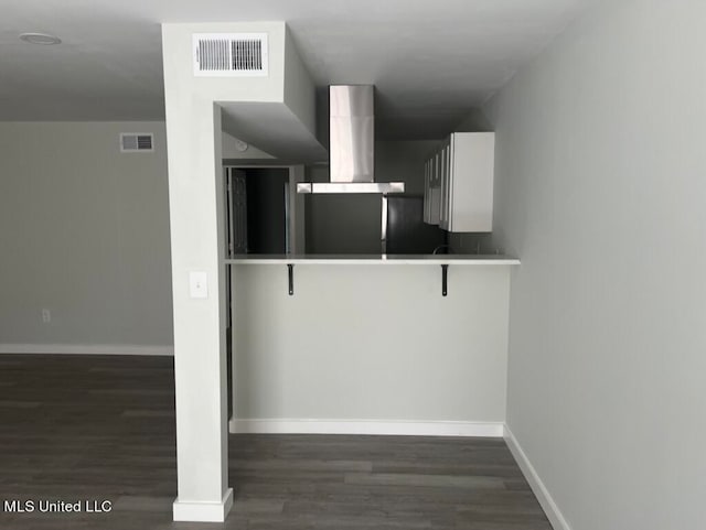 kitchen with kitchen peninsula, a breakfast bar area, white cabinetry, dark hardwood / wood-style floors, and wall chimney exhaust hood