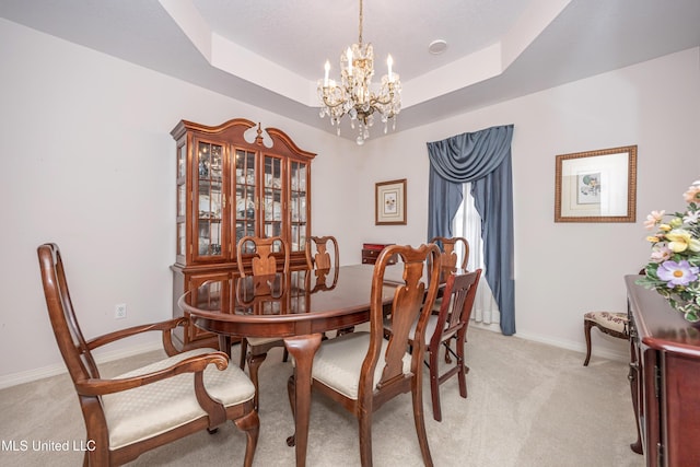 dining space featuring light carpet, a notable chandelier, and a tray ceiling