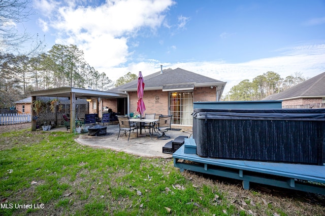 rear view of property featuring a hot tub, a patio area, and a lawn