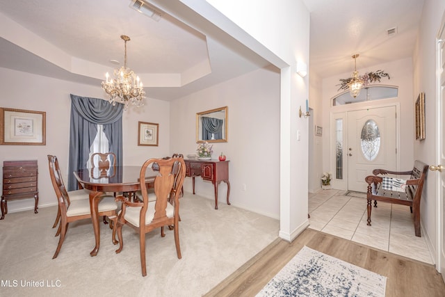 dining area featuring light hardwood / wood-style flooring, an inviting chandelier, and a tray ceiling