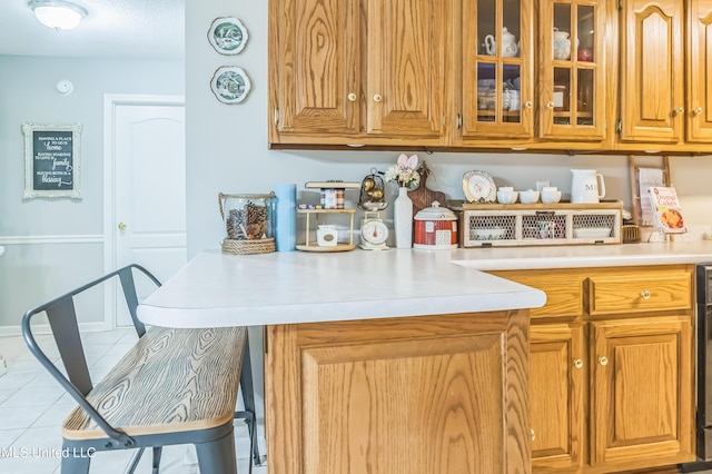 kitchen with light countertops, tile patterned floors, glass insert cabinets, and brown cabinets