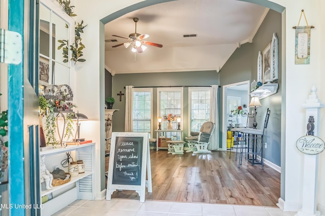 entryway featuring ornamental molding, ceiling fan, vaulted ceiling, arched walkways, and wood finished floors