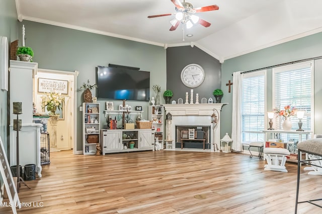 living room with ceiling fan, a fireplace, vaulted ceiling, wood finished floors, and ornamental molding
