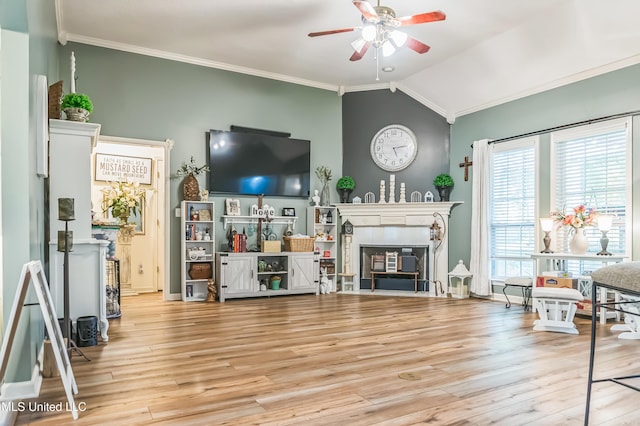 living area featuring a ceiling fan, vaulted ceiling, ornamental molding, wood finished floors, and a fireplace