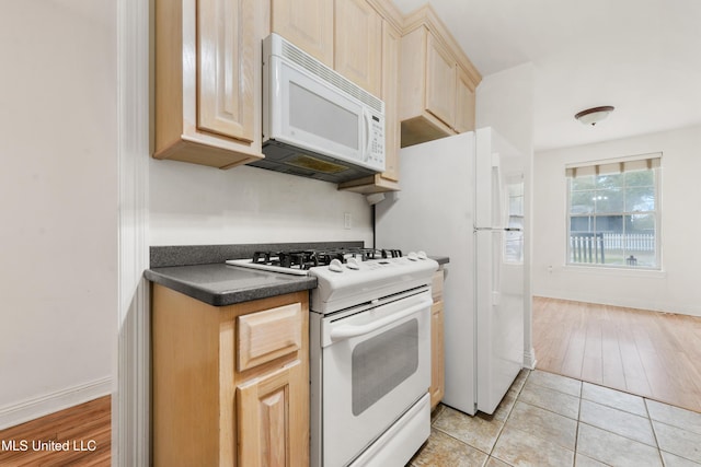 kitchen featuring light tile patterned floors, white appliances, baseboards, light brown cabinetry, and dark countertops